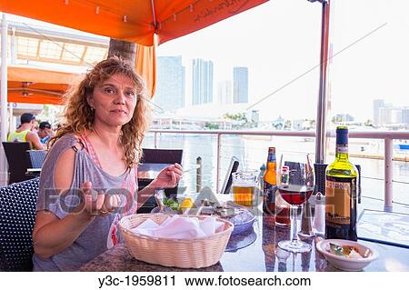 Stock Image - Caucasian woman of 45 years eating fresh raw oysters, Port of Miami, Florida, USA.. Fotosearch