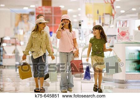 Stock Image - caucasians, hispanic, ages 9 and 10, shopping, talking, cell phone, laughing, young consumers, mall, department store. Fotosearch