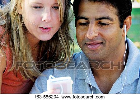 caucasion woman and ethnic man using music device together View Large Photo Image Picture - caucasion woman and ethnic man using music device together. Fotosearch