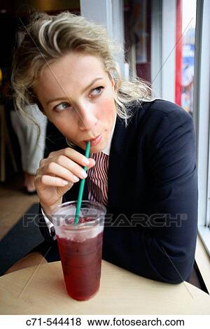 Stock Photo - Caucassian businesswoman at cafe looking off sipping cool drink. Fotosearch