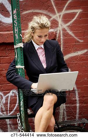 Caucassian businesswoman working on laptop sitting on a bicycle against a graffiti wall View Large Photo Image Picture - Caucassian businesswoman working on laptop sitting on a bicycle against a graffiti wall. Fotosearch