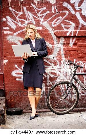 Stock Photo - Caucassian businesswoman working on laptop leaning on graffiti wall. Fotosearch