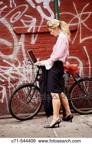 Stock Photo - Caucassian businesswoman working on laptop leaning on bicycle against a graffiti wall. Fotosearch