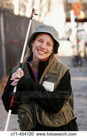 Stock Image - Caussian woman in fishing outfit and fishing pole smiling. Fotosearch