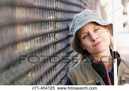 Stock Photography - Caussian woman in fishing outfit and fishing pole smiling leaning on fence. Fotosearch