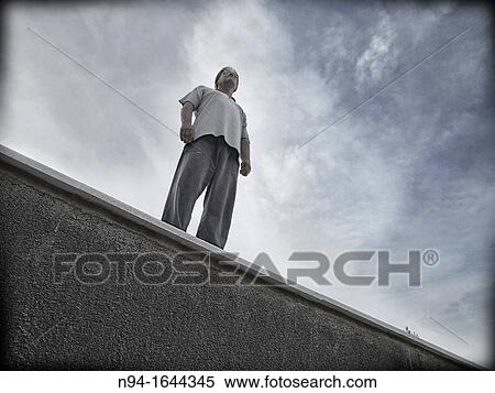 Stock Photography - Challenging single man standing on a ledge.. Fotosearch