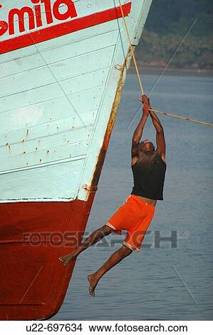 Chapora, Goa India: a young fisherman hanging on a cord of his boat View Large Photo Image Picture - Chapora, Goa India: a young fisherman hanging on a cord of his boat. Fotosearch