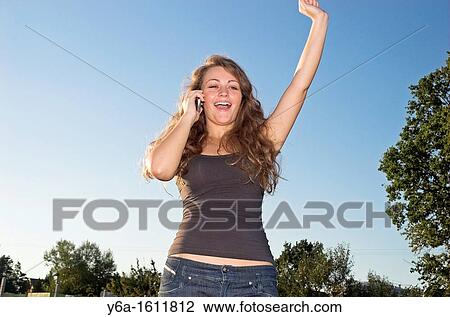 Cheerful young woman with arms raised using a mobile phone View Large Photo Image Stock Image - Cheerful young woman with arms raised using a mobile phone. Fotosearch