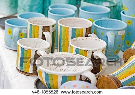 Stock Photograph - Cheery handcrafted ceramic striped cups and saucers Cheery colors of gold, blck, blue and green make attractive casual dinnerware Handcrafted ceramics displayed in public market attract buyers Use of cracked glaze technique Prague, Czech Republic. Fotosearch