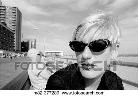 Chic woman in sunglasses sits on bench in New York's Coney Island boardwalk. Model-Released Image. Release Number 1001 View Large Photo Image Stock Photo - Chic woman in sunglasses sits on bench in New York's Coney Island boardwalk. Model-Released Image. Release Number 1001. Fotosearch