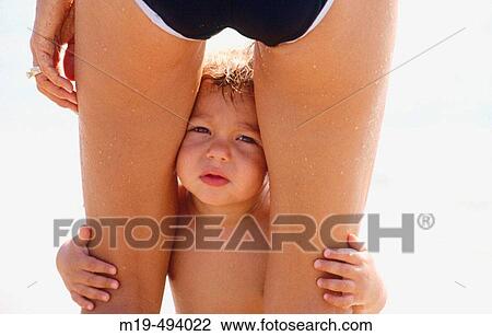Stock Image - child looking between his mothers legs. Fotosearch