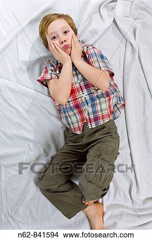 Child lying on the bed that has the hands to the face with a worried expression View Large Photo Image Picture - Child lying on the bed that has the hands to the face with a worried expression. Fotosearch
