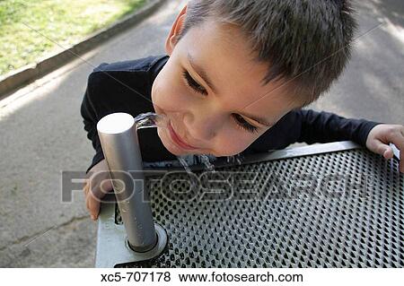 Stock Photo - Child of 7 years old drinking on a source in a park. Fotosearch