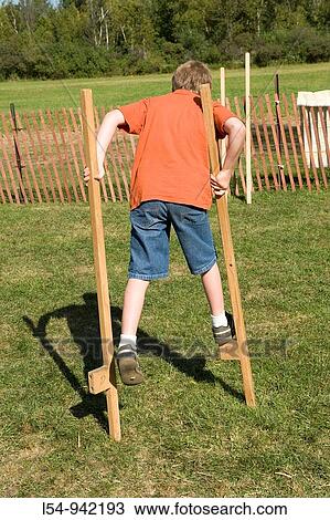 Stock Image - Child walking on wooden stilts learning how to balance on an object. Fotosearch