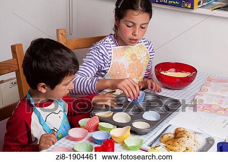 Stock Image - Children applying mixture to baking tin, baking cookies together. Fotosearch