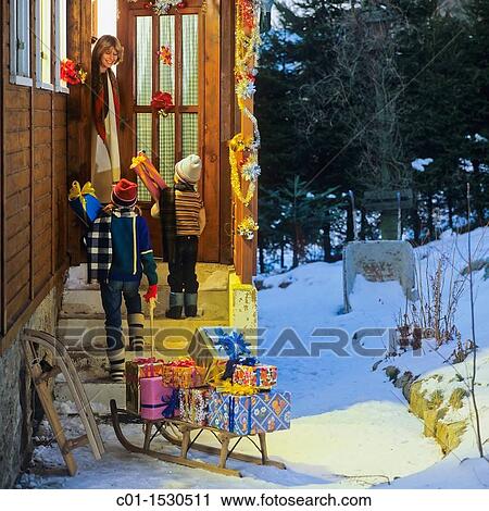 Stock Image - Children giving Christmas presents to woman at cottage doorway. Fotosearch