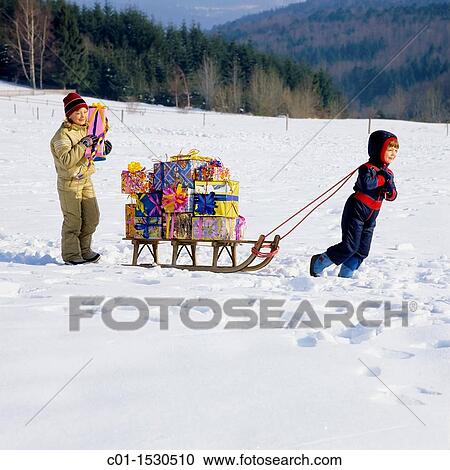 Stock Image - Children with Christmas presents on sledge in snow. Fotosearch