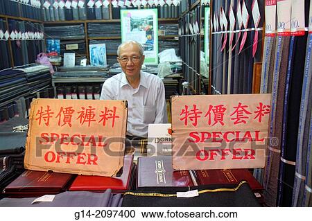 Stock Image - China, Hong Kong, Island, Sheung Wan, Des Voeux Road Central, Western Market, inside, interior, tailor, business suit pants maker, Cantonese Chinese characters h? nz? pinyin, promotion, special offer, Asian, man, senior, manager, owner,.. Fotosearch