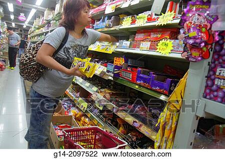 Stock Image - China, Hong Kong, Kowloon, Sham Shui Po, shopping, grocery store, supermarket, sale, display, shelves, Asian, woman, candy,.. Fotosearch