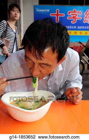 Stock Image - China, Shanghai, Huangpu District, Renmin Road, Yuyuan Garden, Asian, man, eating, chopsticks, noodles, soup, cafe, restaurant, Mandarin symbols, hanzi,. Fotosearch