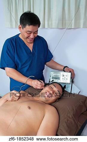 Chinese Acupuncture Doctor giving male patient acupuncture in ear with electronic vibrating stimulation with Stim Flex 400 machine View Large Photo Image Stock Photo - Chinese Acupuncture Doctor giving male patient acupuncture in ear with electronic vibrating stimulation with Stim Flex 400 machine. Fotosearch