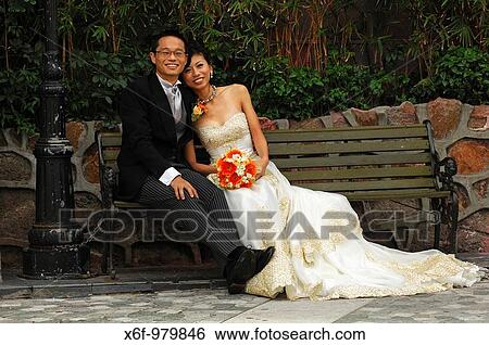Chinese bride and groom in long wedding gown and dark suit sitting on a bench, Chinese Hong Kong, China View Large Photo Image Stock Photograph - Chinese bride and groom in long wedding gown and dark suit sitting on a bench, Chinese Hong Kong, China. Fotosearch