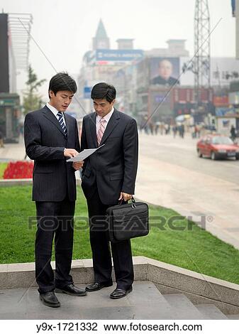 Stock Image - Chinese business men look at a sheet of paper to help one another. Fotosearch