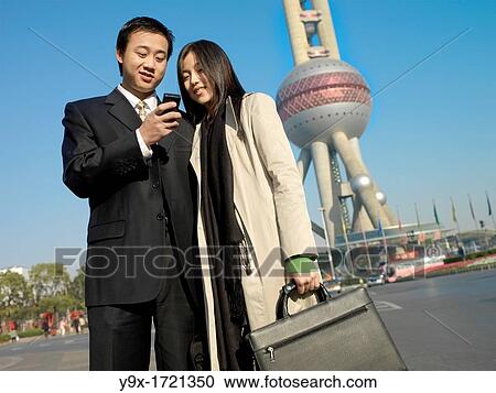 Chinese couple standing before the Pearl Tower in Shanghai, China using their phones to communicate with people View Large Photo Image Stock Image - Chinese couple standing before the Pearl Tower in Shanghai, China using their phones to communicate with people. Fotosearch