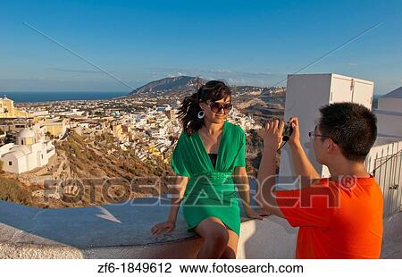 Chinese couple tourists taking picture of themselves overlooking Fira at sunset in Santorini Greece in the Greek Islands View Large Photo Image Stock Image - Chinese couple tourists taking picture of themselves overlooking Fira at sunset in Santorini Greece in the Greek Islands. Fotosearch