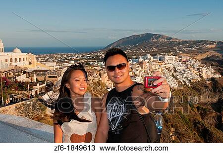 Chinese couple tourists taking picture of themselves overlooking Fira at sunset in Santorini Greece in the Greek Islands View Large Photo Image Stock Image - Chinese couple tourists taking picture of themselves overlooking Fira at sunset in Santorini Greece in the Greek Islands. Fotosearch