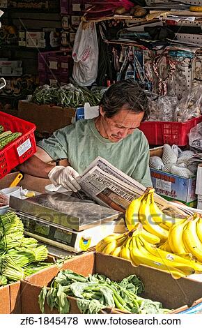 Stock Photo - Chinese man reading China newspaper in market of fruit in Chinatown Los Angeles California on N Broadway Street. Fotosearch