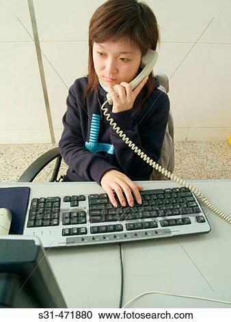 Stock Image - Chinese secretary at work answering the phone. Fotosearch