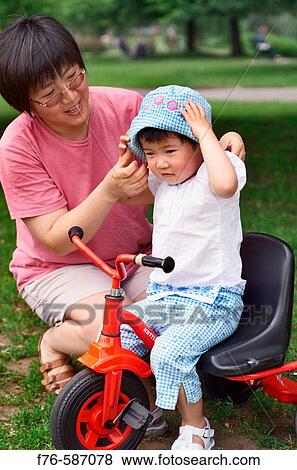 Chinese woman / mother putting hat on her 3 year old girl as she rides her tricycle. View Large Photo Image Stock Photo - Chinese woman / mother putting hat on her 3 year old girl as she rides her tricycle.. Fotosearch