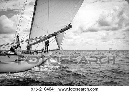 Stock Image - Classic sailboat in a regatta with sailors in the background at the Mediterranean sea, Menorca, Balearic Islands, Spain.. Fotosearch