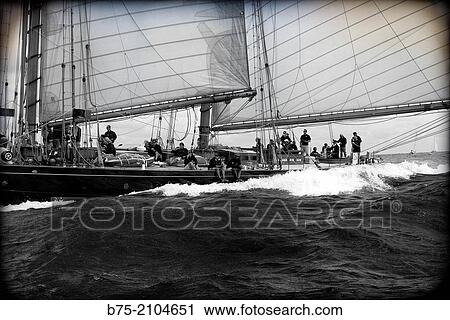 Stock Image - Classic sailboat in a regatta with sailors in the background at the Mediterranean sea, Menorca, Balearic Islands, Spain.. Fotosearch