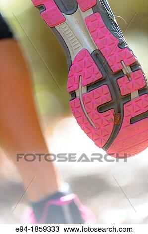 Stock Image - Close shot of the sole of a running shoe on a woman running through a forest. Fotosearch
