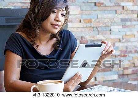 Stock Image - Close up of a African American young woman hand holding an iPad at a restaurant or cafe. Fotosearch