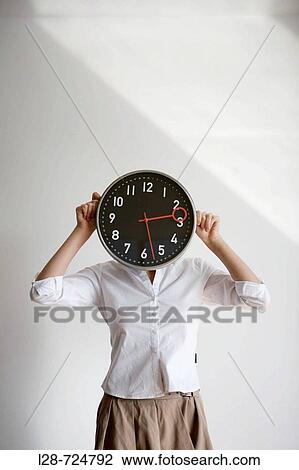 Stock Image - Close-up of a businesswoman holding a clock in front of her face. Fotosearch