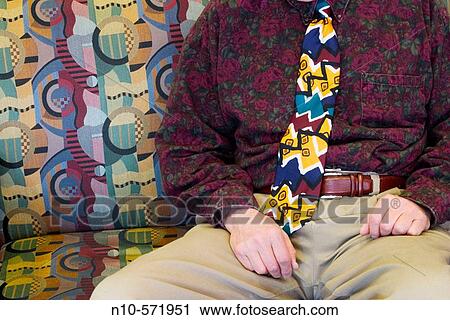 Stock Image - Close-up of a man wearing a colorful shirt and tie, sitting on a colorful sofa. Fotosearch