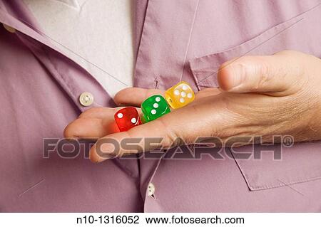 Stock Image - Close-up of a man's hand holding three dies. Fotosearch