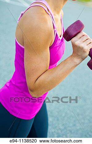 Stock Image - Close up of a thirty year old woman's flexed bi-cep pumping a dumbbell.. Fotosearch