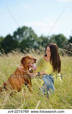 Stock Photo - Close-up of a Woman with a Hungarian or Magyar Vizsla (Vizsla) on a meadow in spring.. Fotosearch