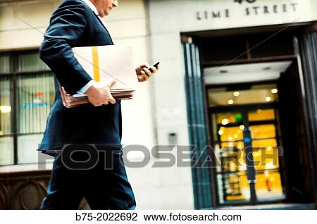 Close-up of an executive with folder and mobile phone in hand walking down a street in the City of London, England, UK View Large Photo Image Stock Image - Close-up of an executive with folder and mobile phone in hand walking down a street in the City of London, England, UK. Fotosearch