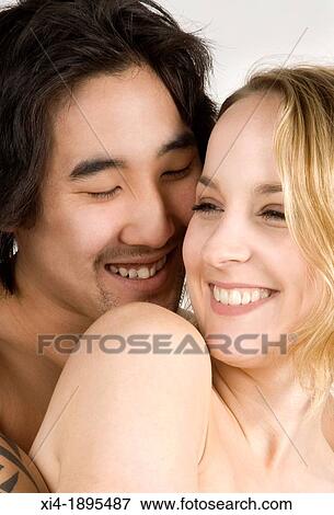 Close-up of Asian & caucasian couple hugging He is close to her cheek with a smile and she is welcoming the hug They both are showing bare shoulders White background View Large Photo Image Stock Photo - Close-up of Asian & caucasian couple hugging He is close to her cheek with a smile and she is welcoming the hug They both are showing bare shoulders White background. Fotosearch