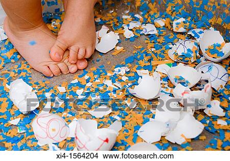 Picture - Close up of baby feet in the middle of broken easter eggs. Fotosearch