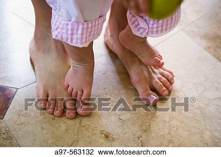 Stock Image - Close-up of mother and infant girl's barefeet. Infant is standing on mother's feet.. Fotosearch