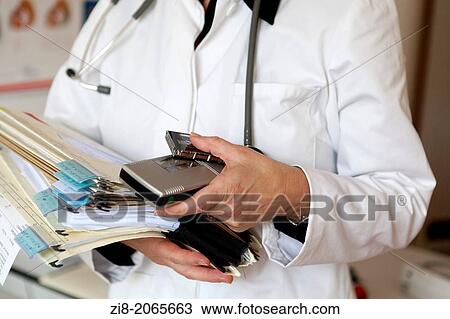 Stock Image - Close-up of overworked doctor holding patient files.. Fotosearch