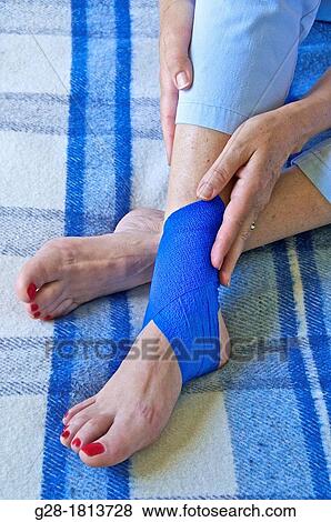 Close up of senior woman sitting on her bed, and holding her leg with a blue bandage around her twisted ankle View Large Photo Image Stock Photo - Close up of senior woman sitting on her bed, and holding her leg with a blue bandage around her twisted ankle. Fotosearch