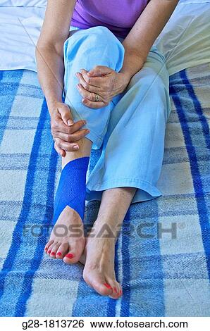 Close up of senior woman sitting on her bed, and holding her leg with a blue bandage around her twisted ankle View Large Photo Image Stock Photograph - Close up of senior woman sitting on her bed, and holding her leg with a blue bandage around her twisted ankle. Fotosearch
