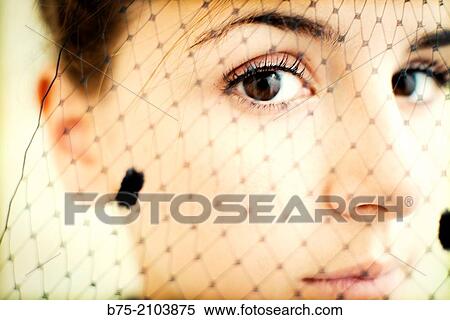 Stock Photography - Close-up of teenager girl looking at the camera with a veil in front of her face.. Fotosearch